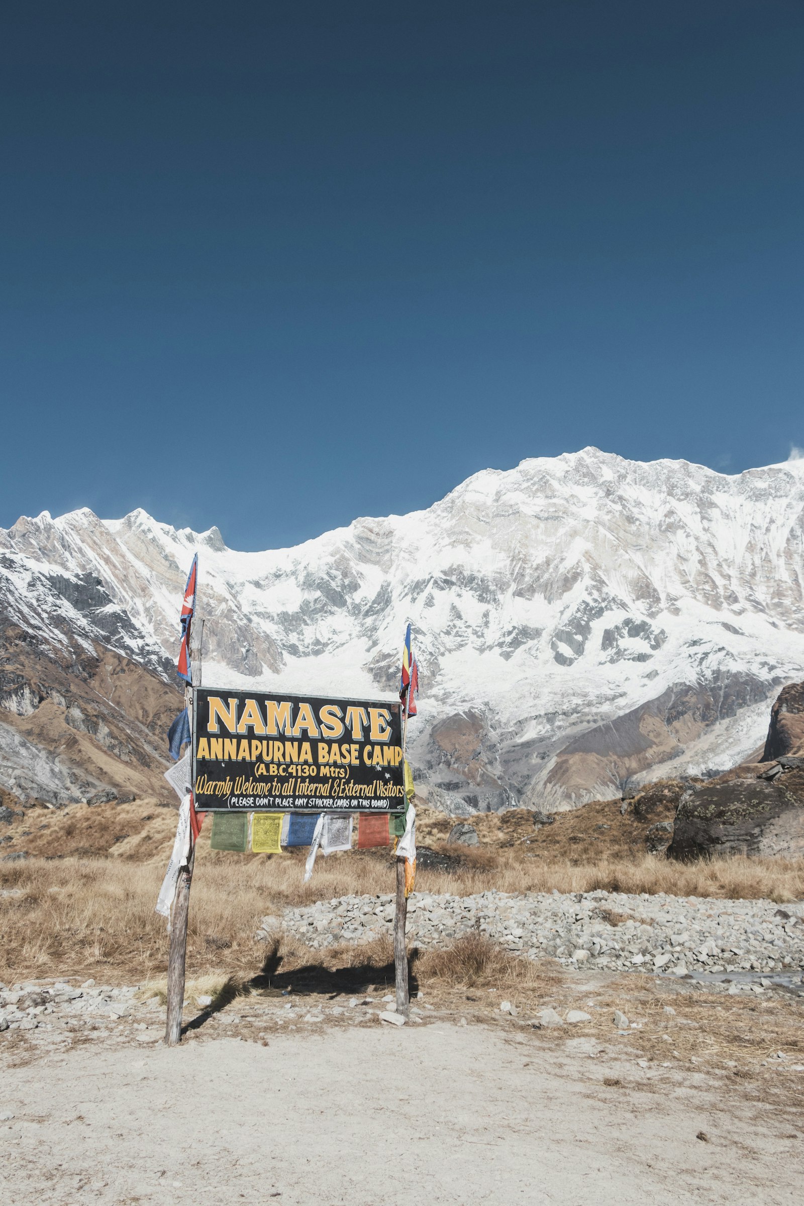 The Annapurna Base Camp sign at 4,130 m, with prayer flags and the sanctuary peaks behind it